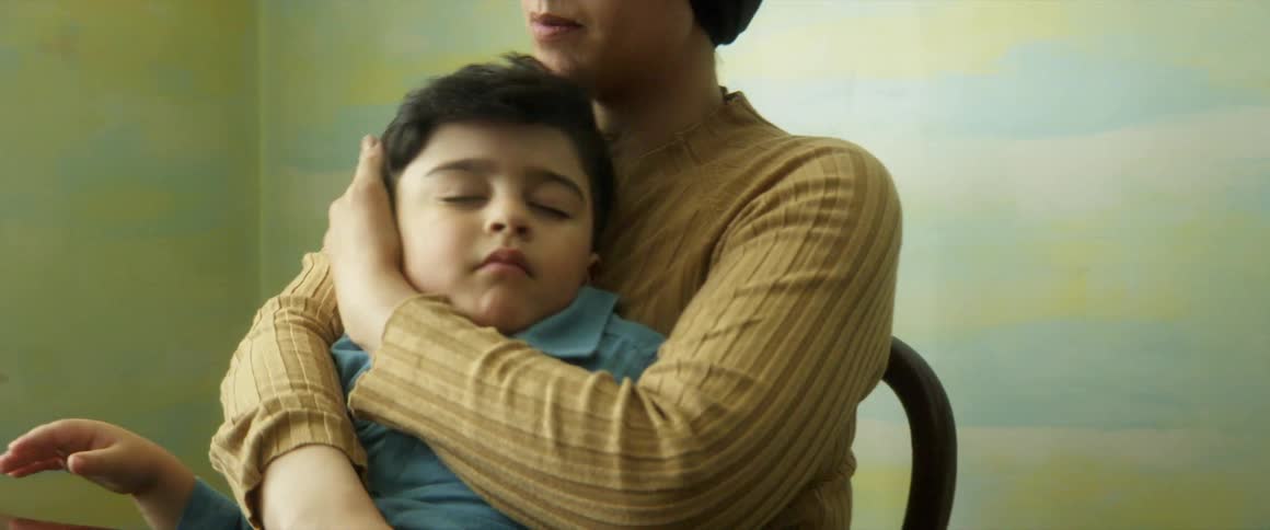 A mother holds her sleeping son in her lap as she video chats on a tablet
