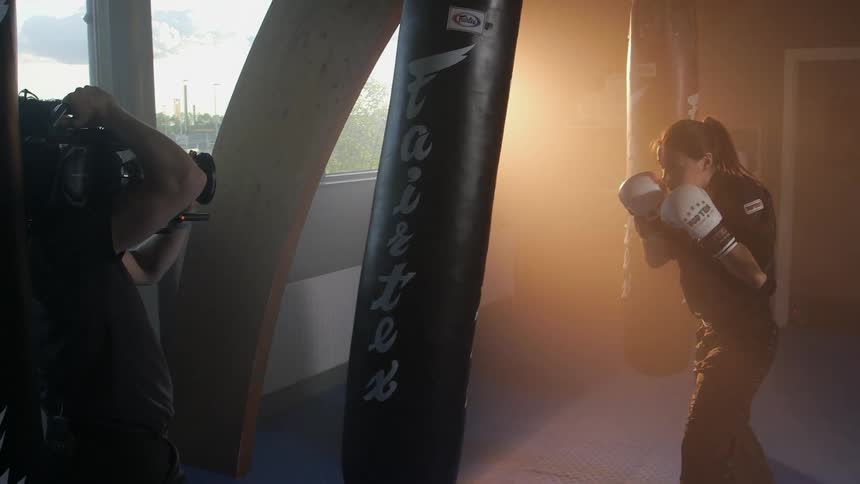 A woman is punching a heavy bag while being filmed