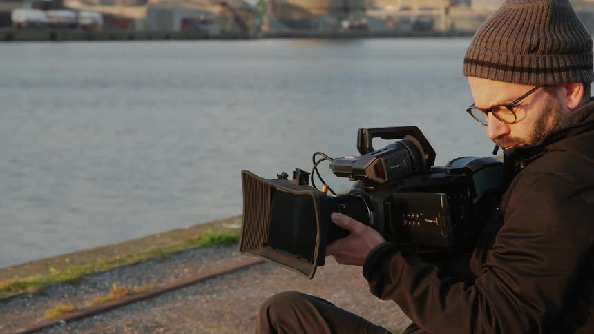A man filming near a river that runs through an urban area