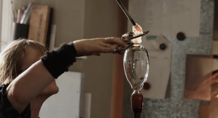 A woman places and snips blown glass