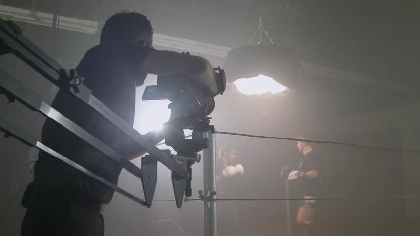 A cameraman films two fighters sparring in a boxing ring