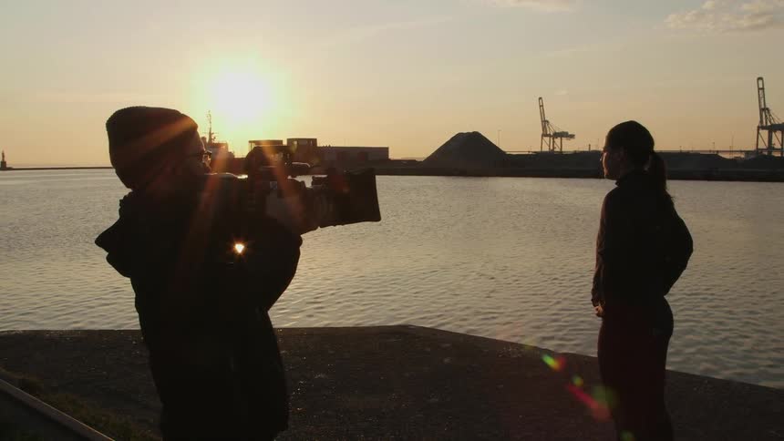 A woman is filmed by the water at sunset
