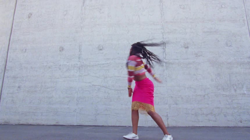 A woman with a sweater and skirt dancing in front of a wall
