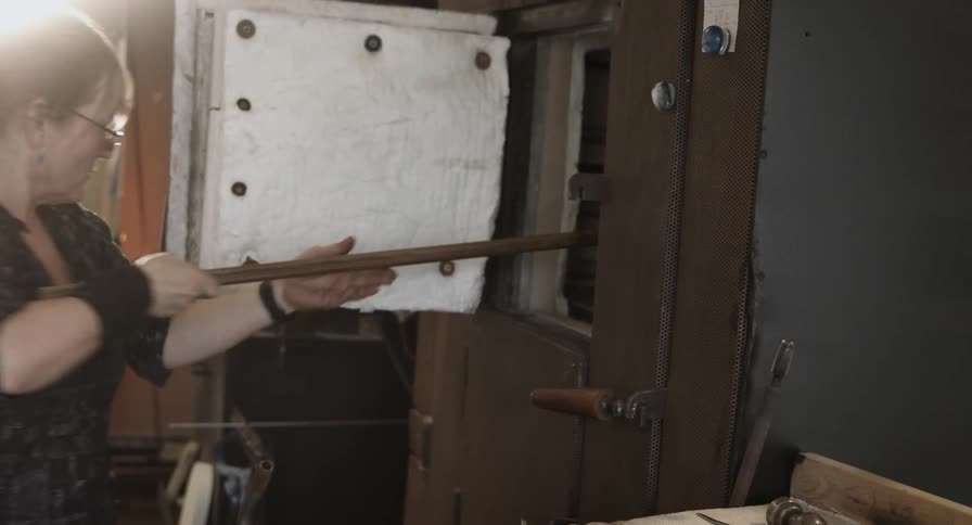 Woman using tongs places a hot glass into a cooling cabinet