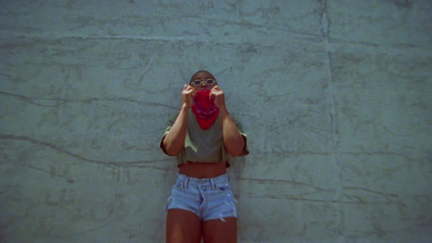 Woman reclined on a concrete wall pulls up a red bandan over her face