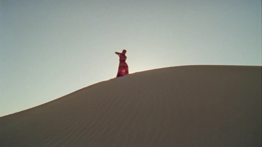 A woman dances at the top of a sandy hill