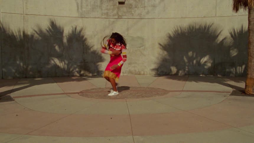 A woman dancing between two palm trees on a pink and walk concrete circular surface outdoors