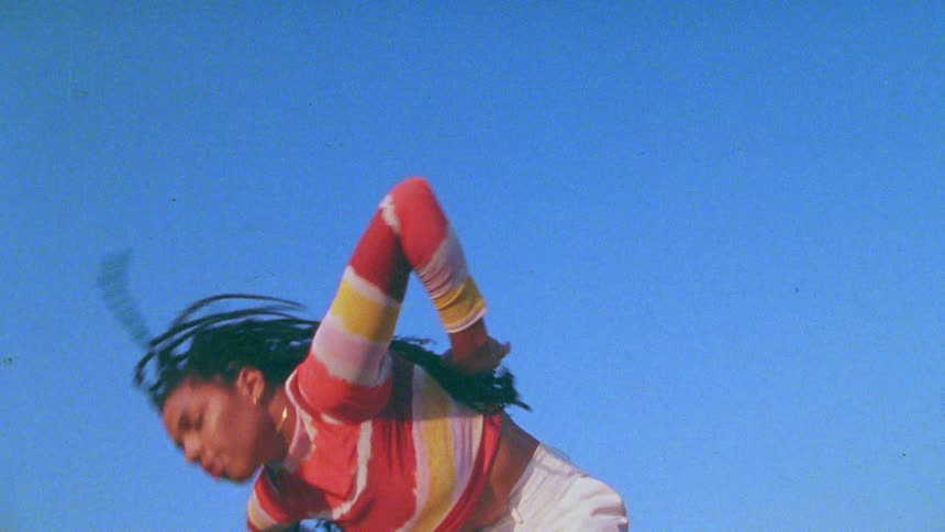 Young long haired woman energetically dancing in front of a clear blue sky