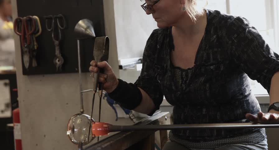 A female artisan rolls a stick with hot glass on the end