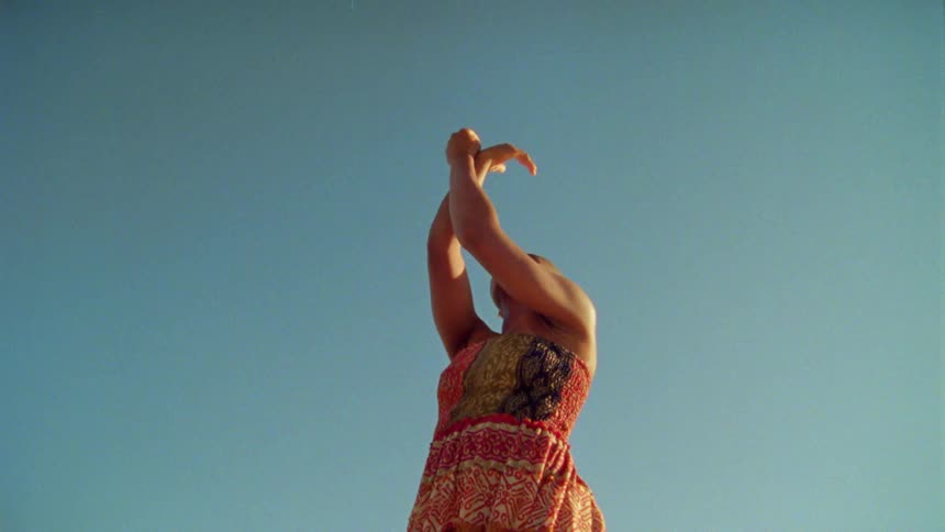 Woman wearing patterned sleeveless dress dance under clear blue sky