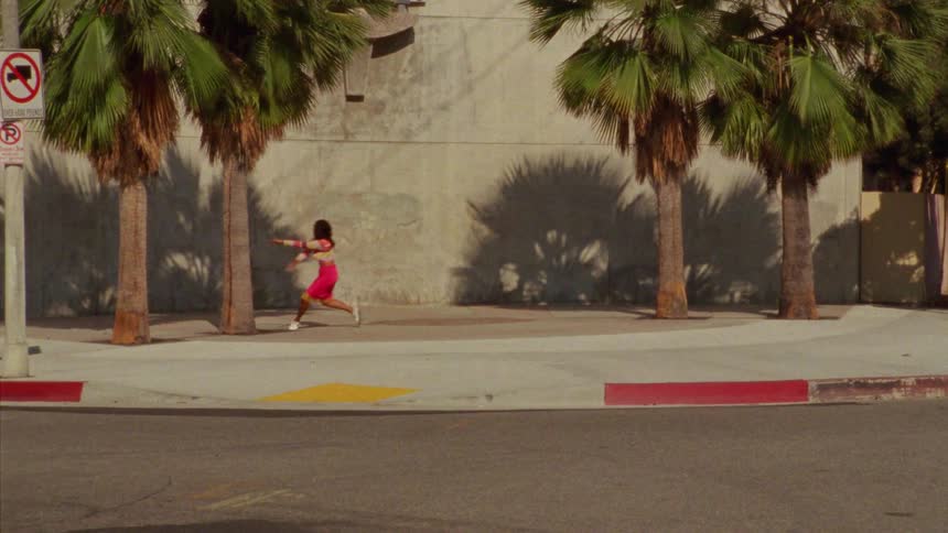 A young long haired woman energetically dancing in front a concrete wall surrounded by palm trees