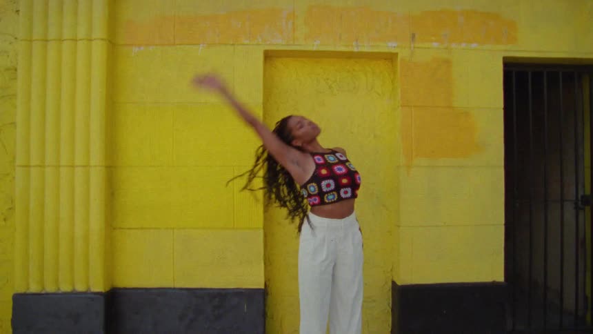 A young long haired woman dancing in front or a yellow wall