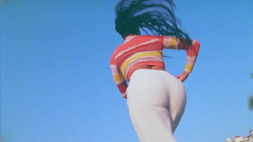 A young woman dances outdoors under a clear blue sky