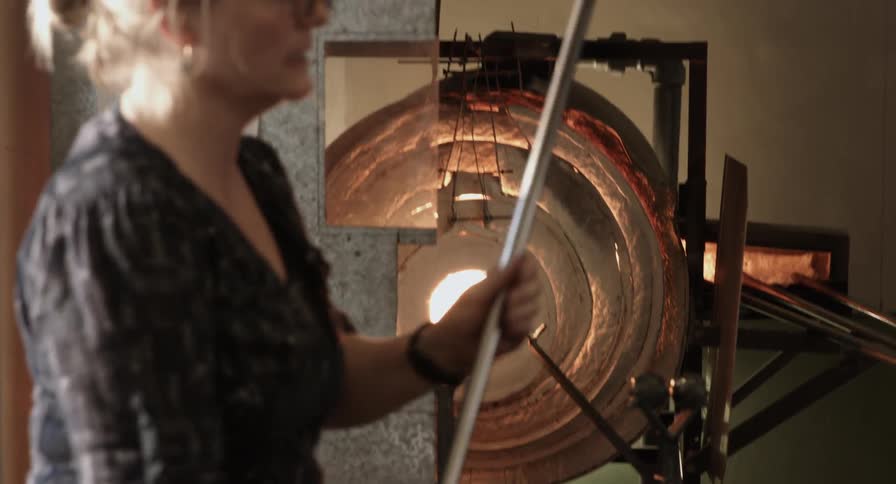 A woman is spinning glass in an oven