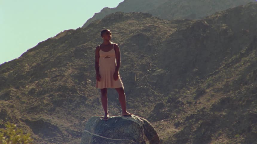 A young woman stands on a rock and looks out in the distance