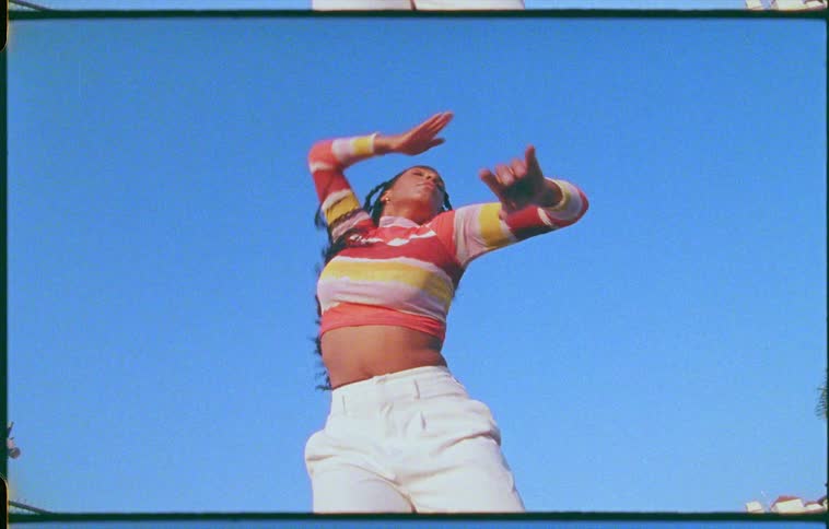 A black female with long braids is dancing under a clear blue sky