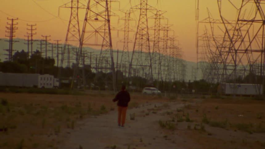 A person walking near power lines and transmission towers at sunset