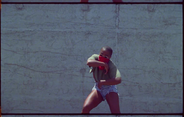 Woman wearing bandana over her face and shorts dances outside