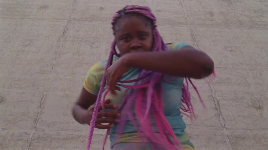 Young woman with long pink hair dances outdoors looking at the camera