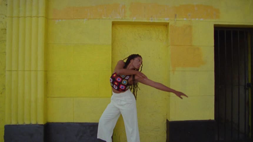 A woman does a modern style dance in front of a concrete wall painted yellow
