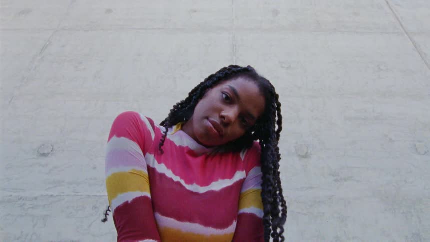 Woman leaning against a concrete wall walks forward to look at the camera
