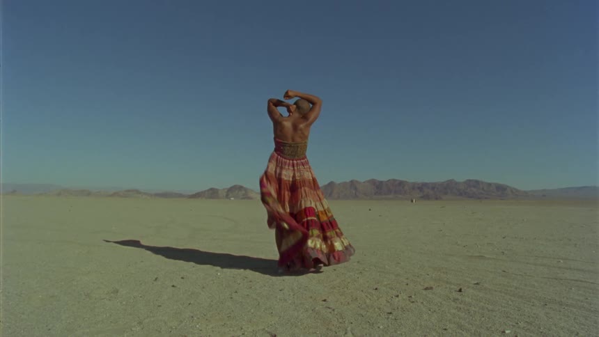 Woman wearing a dress stretches her arms up while standing on the sands of a desert
