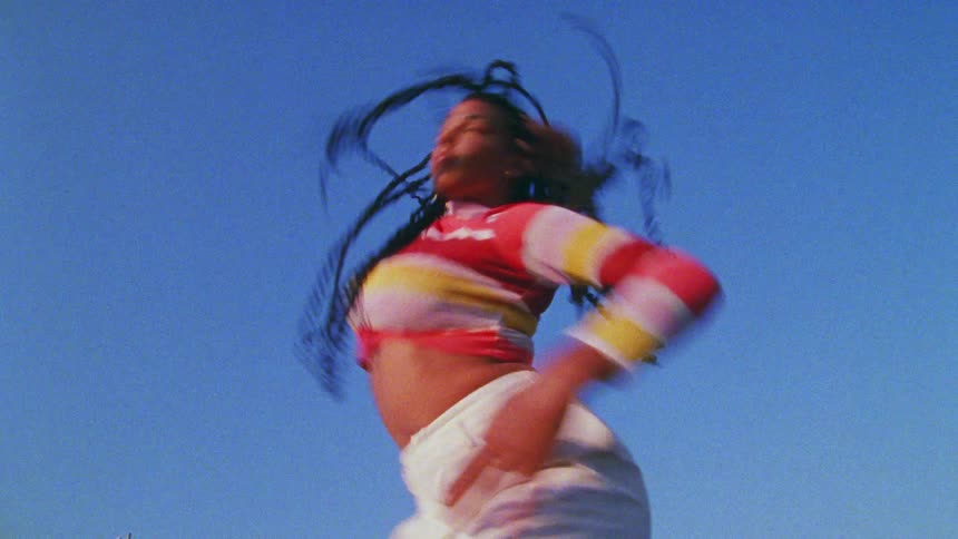 A woman with a sweater dancing with the sky and clouds above