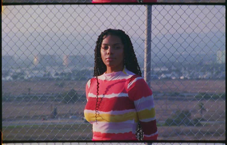 Young woman standing in front of a wire fence looking at the camera