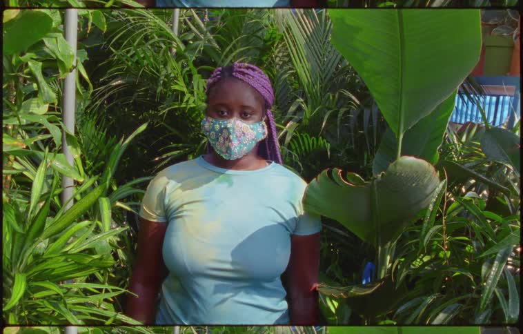 Footage of a teenage girl standing in plants with a mask on