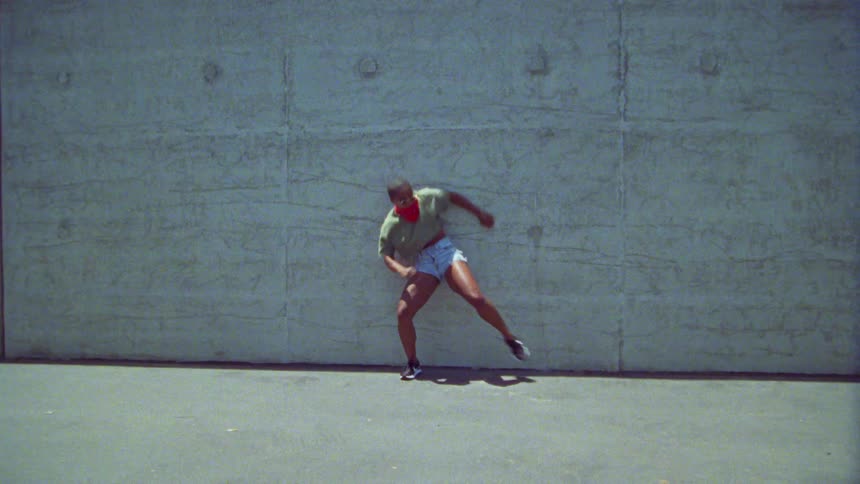 A woman against a concrete wall outdoors performing dance moves at daytime