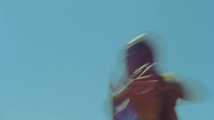 Young bald woman energetically dancing in front of a clear blue sky