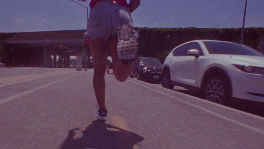 Black woman with shorts runs along highway next to cars