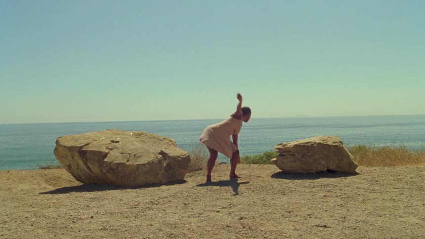 A woman in a pink dress dancing between two rocks in the coast near the ocean