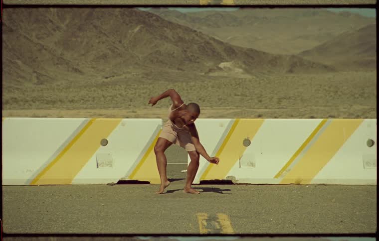 Woman dancing in front of concrete barriers in a rural road in the desert