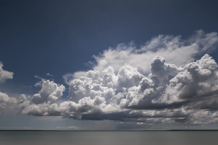 Cumulus clouds above an ocean move across the sky on a very cloudy day
