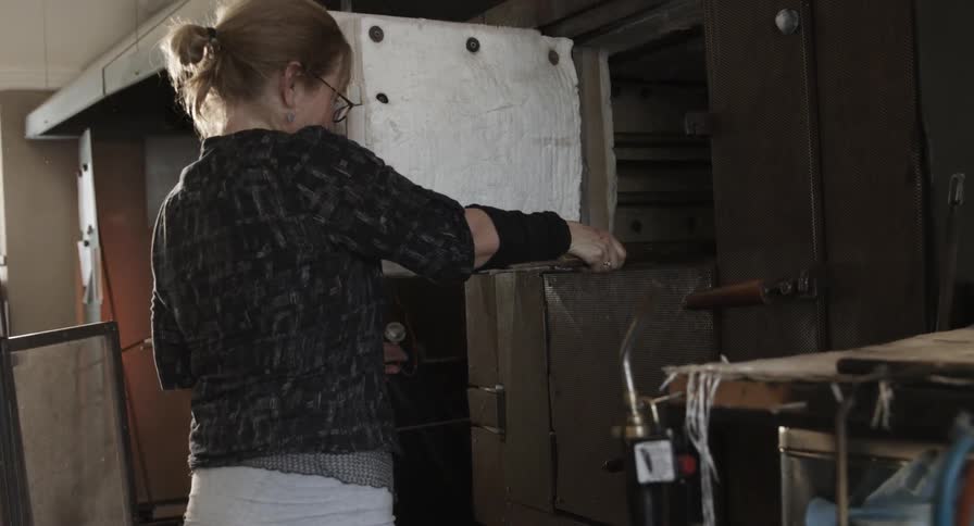 A female glassmaker uses a rod to place a glass plate in an oven
