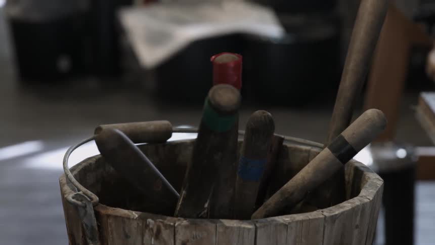 Tools sit in a wooden bucket in a room in daylight