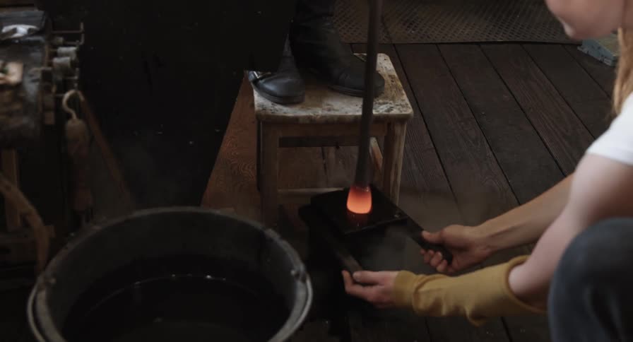 A woman holds a smoking mold for a glass blower