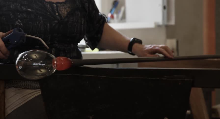 A glass worker crafts glass on a steel rod