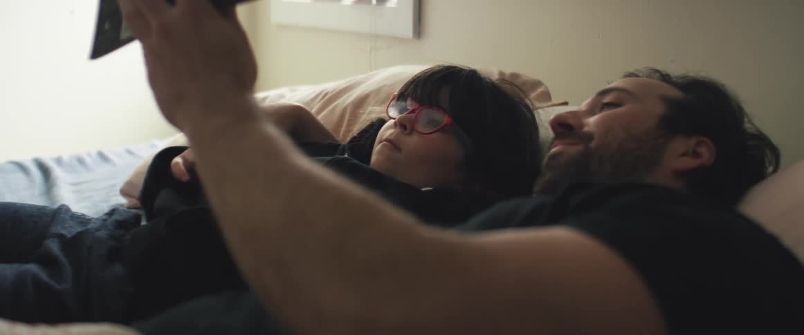 A man and a boy laying on a bed in a bedroom looking at a tablet