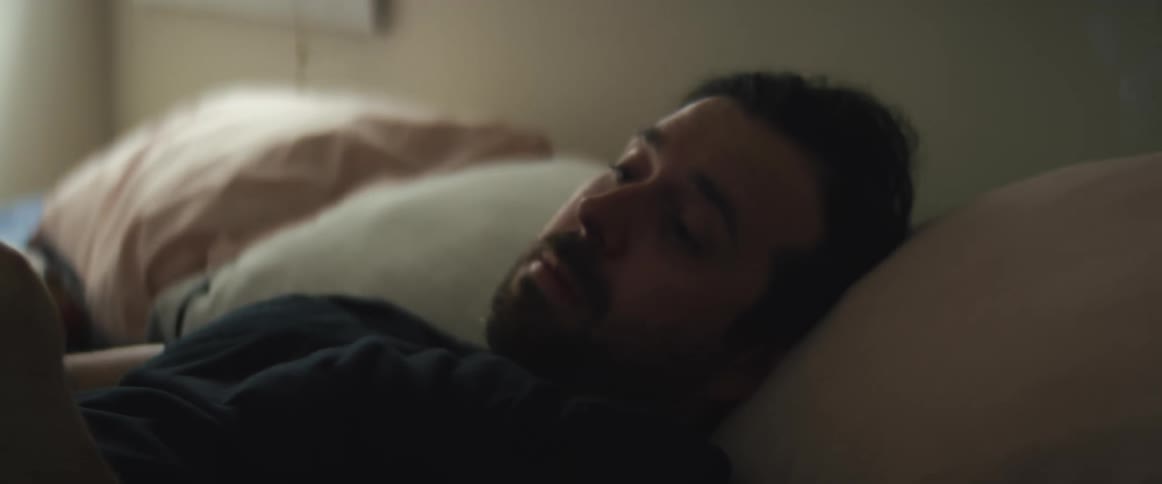 A man laying in bed rubs his face then picks up his smart phone and begins to look at it