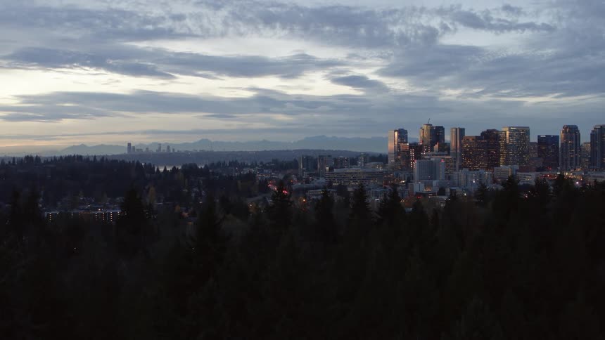 Subtle ascent from urban woodlands to reveal downtown Bellevue with the Olympic Mountains and Seattle skyline in the distance