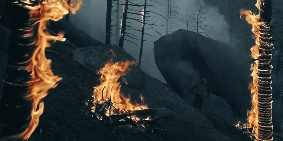 A mountain biker hits a rock wall ride in a burning forest