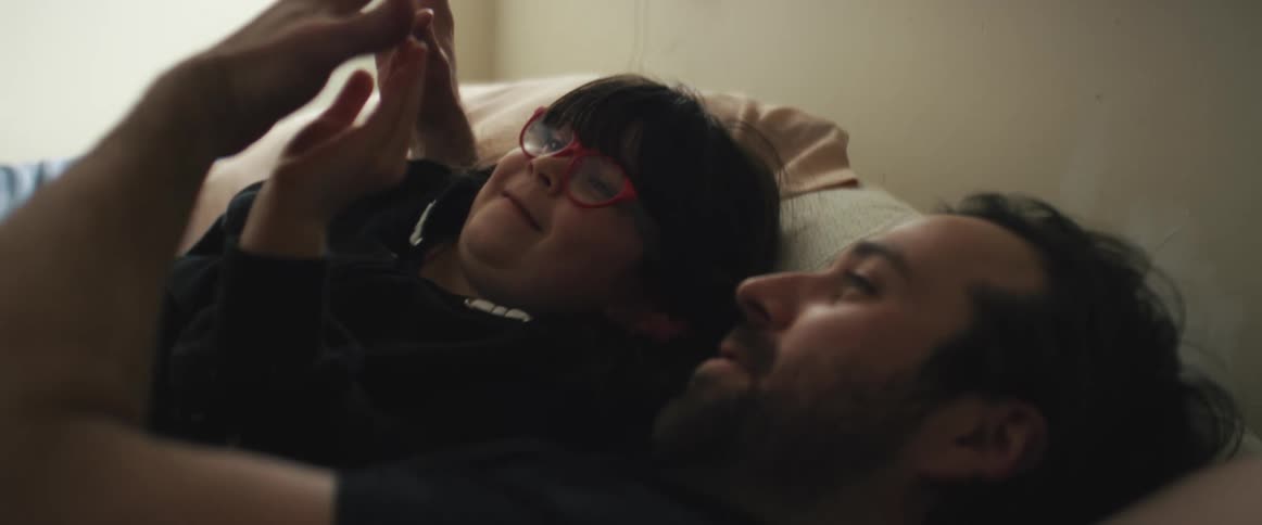 A man and a boy with glasses laying on a bed with pillows