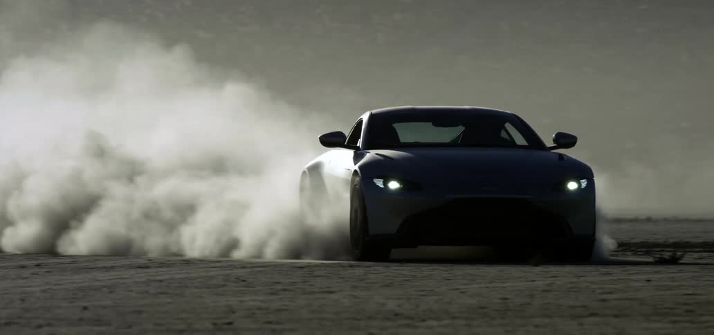 Sports car speeds across flat ground throwing smoke and dust into the air