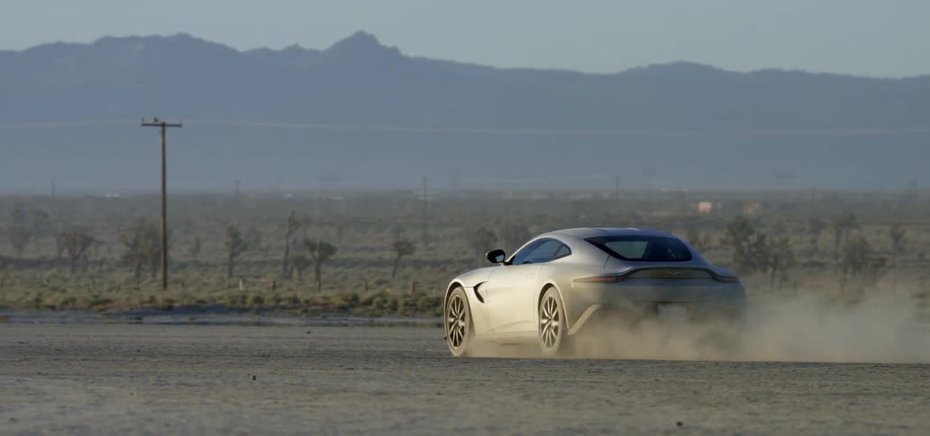 Sports car leaving a dust trail while driving on the desert at sunset