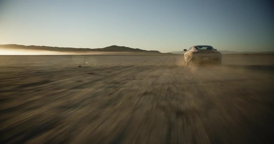 A silver sports car driving off road in the desert kicks up dust towards the camera and speeds off