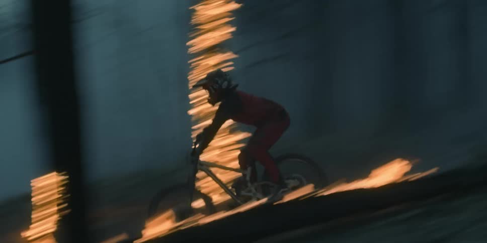 Cyclist driving a mountain bike over burning logs in a forest at sunset