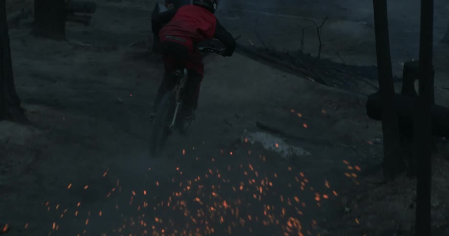 A man jumps his bicycle with burning ash cloud behind him.