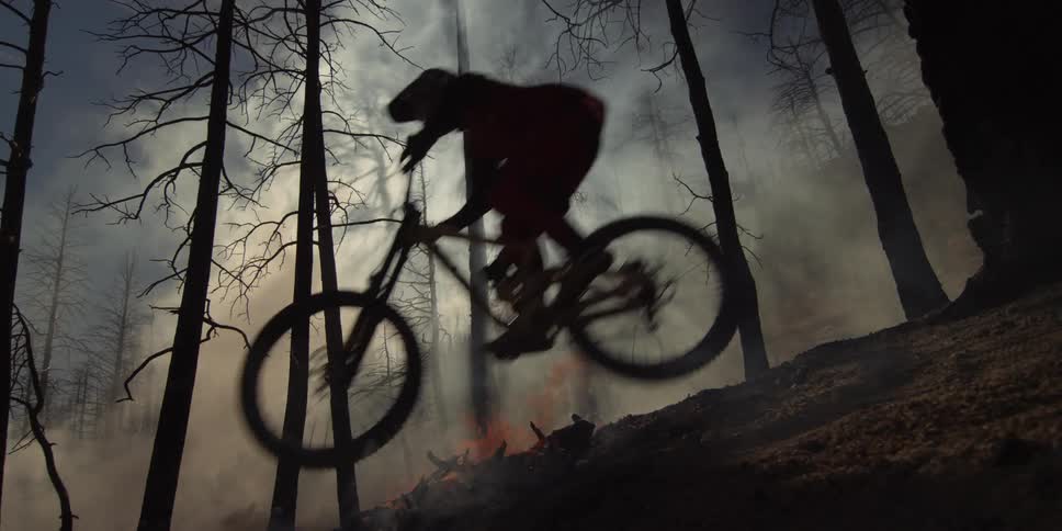 Cyclist riding a mountain bike over a mound of burning ashes in a forest